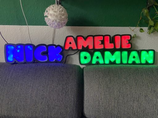 Beleuchtete Buchstabenformen: "KICK", "AMELIE", "DAMIAN", in verschiedenen Farben.
