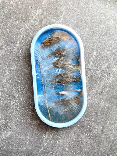 Zarte Gräser unter einem blauen Himmel in ovaler Rahmenpräsentation.